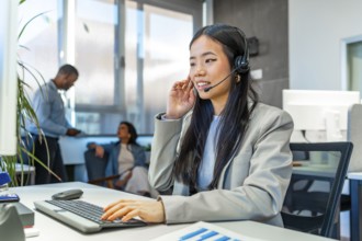 Young asian operator wearing headset working on computer keyboard in a coworking office with