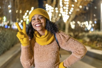 Portrait of a smiling young woman wearing yellow winter clothes showing victory sign with fingers
