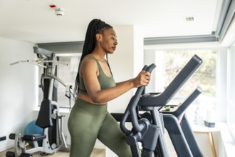 Businesswoman exercising on elliptical cross trainer in hotel gym, maintaining healthy lifestyle