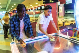 Two young men concentrating on playing air hockey in a vibrant entertainment center, enjoying a