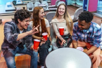 Four young multiethnic friends are laughing and having fun while sitting in a bowling alley,