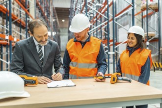 Manager signing delivery notes in a logistics warehouse, assisted by two warehouse workers using