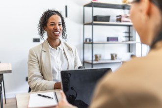 Two businesswomen smiling and discussing strategy during a meeting in the office using a laptop