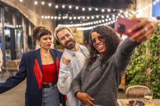 Latin woman taking selfie with friends at night party in an outdoor terrace of a bar