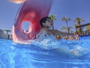 Young boy sliding joyfully into a pool at a vibrant water park, delighting in the excitement of