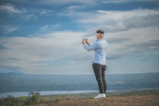 Young man taking photos with cell phone at a natural viewpoint. Tourist taking photos with phone at