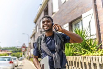 Confident young casual african businessman using phone walking along a residential street