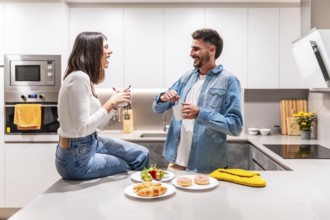 Young couple laughing and talking while having breakfast and coffee in their modern kitchen