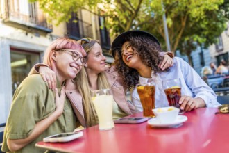 Diverse female modern friends hugging and smiling sitting in an outdoor bar terrace