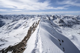 Tracks in the snow on a narrow mountain ridge in winter, summit of Piz Grialetsch, view of mountain