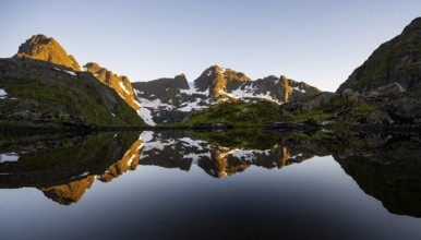 Rocky mountain peaks reflected in a small pond, mountain landscape with alpenglow at sunrise, at