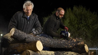 ©Udo Rein, Two men cutting thick logs with a chainsaw at night, Easter fire Psinthos, Holy