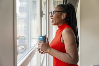 Happy businesswoman enjoys a coffee break in her hotel room, looking out the window and smiling