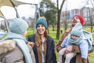 Happy parents holding their baby, laughing and talking with their other child in a park during
