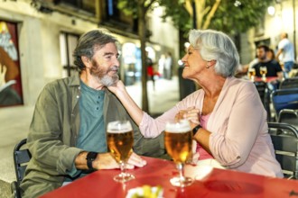 Senior woman caressing the face of her husband sitting on an outdoor terrace drinking beer at bar