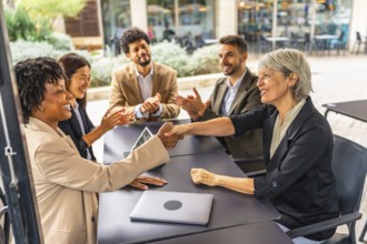 Businesswomen closing deal shaking hands in a cafeteria while colleagues applauding