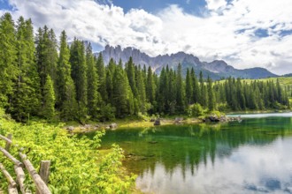Emerald waters reflecting latemar mountain range and lush forest in the italian dolomites on a