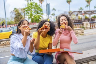 Female multi-ethnic friends having fun eating pizza sitting outdoors in the city
