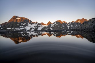 Rocky mountain peaks reflected in a small pond, mountain landscape with alpenglow at sunrise, at