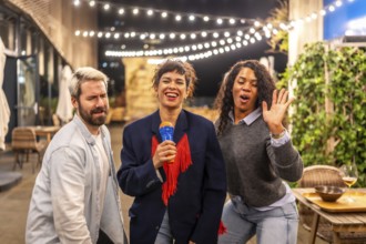 Happy diverse friends dancing and singing karaoke at night party in the roof terrace of an urban