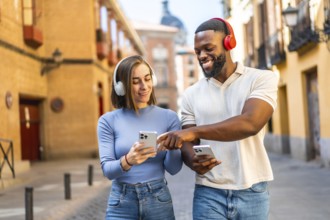 Happy multi-ethnic couple listening to music and using mobile phone walking in the city