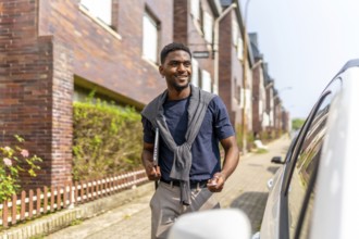 African young businessman going to work by car opening it by remote control while carrying laptop