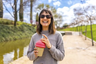 Young woman smiling and holding a reusable cup with a straw, enjoying a refreshing drink in a sunny