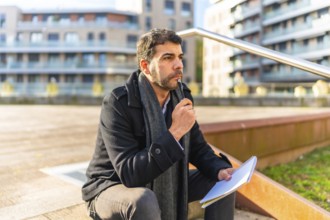 Pensive casual businessman writing notes sitting on urban stairs in autumn