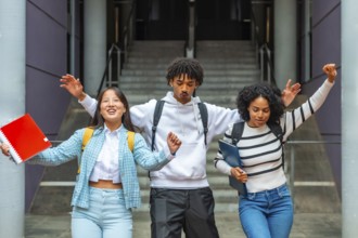Three multi-ethnic female and male students having fun celebrating and dancing outside the