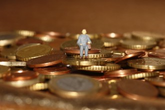 Miniature man sitting among euro coins, North Rhine-Westphalia, Germany, Europe