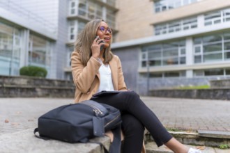 Side view of a latin businesswoman talking to the smartphone sitting in the street