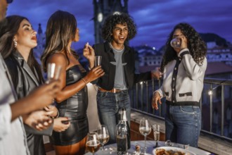 Happy multiracial stylish friends dancing and drinking champagne during night party on roof