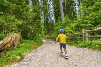 Child running along a gravel path through a lush forest near lake carezza in the italian dolomites,