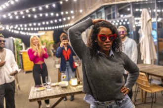 Sensual latin woman with sunglasses and casual winter clothes dancing next to friends at night