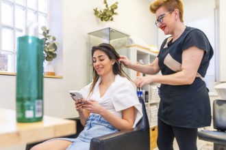 Hairdresser combing the hair of a client while she using mobile phone