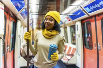 Smiling woman wearing yellow woolen hat and gloves holding a reusable mug while standing inside a