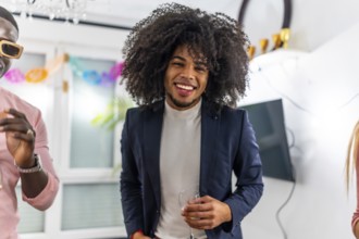 Latin cheerful man with curly hair smiling at camera during home party with friends