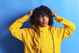 Young woman with curly hair wearing a yellow raincoat adjusting the hood while looking away on a