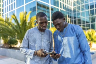 Two senegalese businessmen wearing traditional dashiki attire are using smartphones in front of a