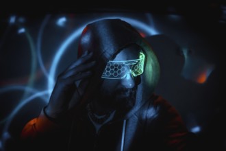 Bearded hacker adjusting futuristic glasses and touching his head in dark room with light effects