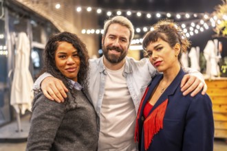 Portrait of three multi-ethnic friends embracing and smiling at camera at night party