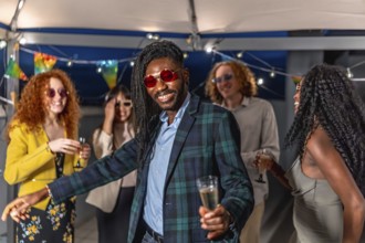 Portrait of a happy young african stylish man dancing with friends at night roof party