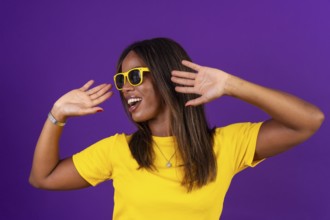 Studio portrait with purple background of an african cool urban woman with sunglasses dancing