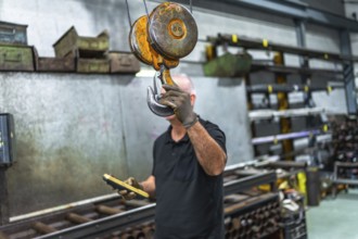 Mature caucasian man holding the hook of an industrial crane while operating in a factory