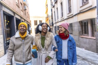 Three happy friends are walking arm in arm down a city street, laughing and enjoying each other's
