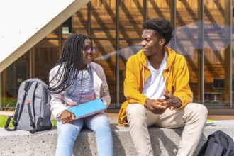 Two young African american students chatting relaxed outside the university sitting together under
