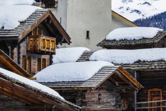 Old wooden houses with snow-covered roofs and the Saint Theodule church in the historic village