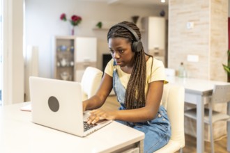 Young student concentrating on her laptop, wearing headphones, diligently working on school