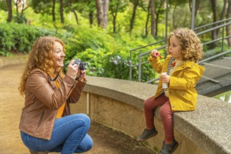 Mother taking portraits to her daughter blowing bubbles sitting on a park