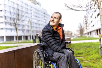 Young man using wheelchair smiling while enjoying a day out in an urban park, promoting inclusion